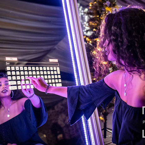 Young woman using an interactive mirror photo booth with a touchscreen keyboard at an event.