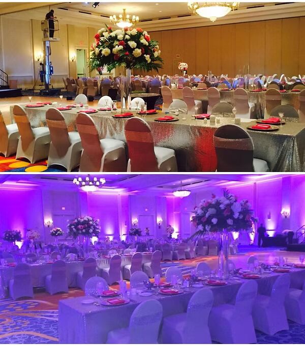 Elegant banquet hall set up for a wedding or event with silver tablecloths, chair covers, floral centerpieces, and dramatic lighting.