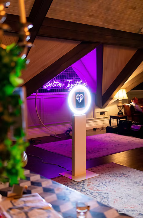 Ring light photo booth set up in a decorated event space with a neon sign reading 'Better Together' glowing in the background.