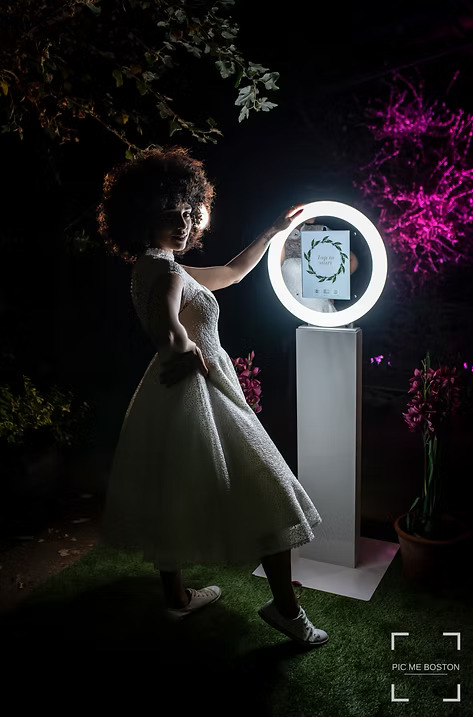Bride in a white dress posing outdoors at night with a glowing ring light photo booth station.