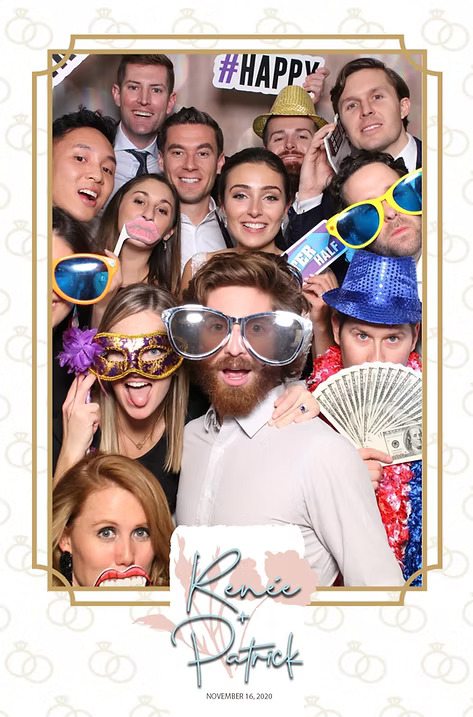 Large group of wedding guests posing at a photo booth with fun props including oversized glasses, hats, money fan, and signs, framed with the names Renée and Patrick.